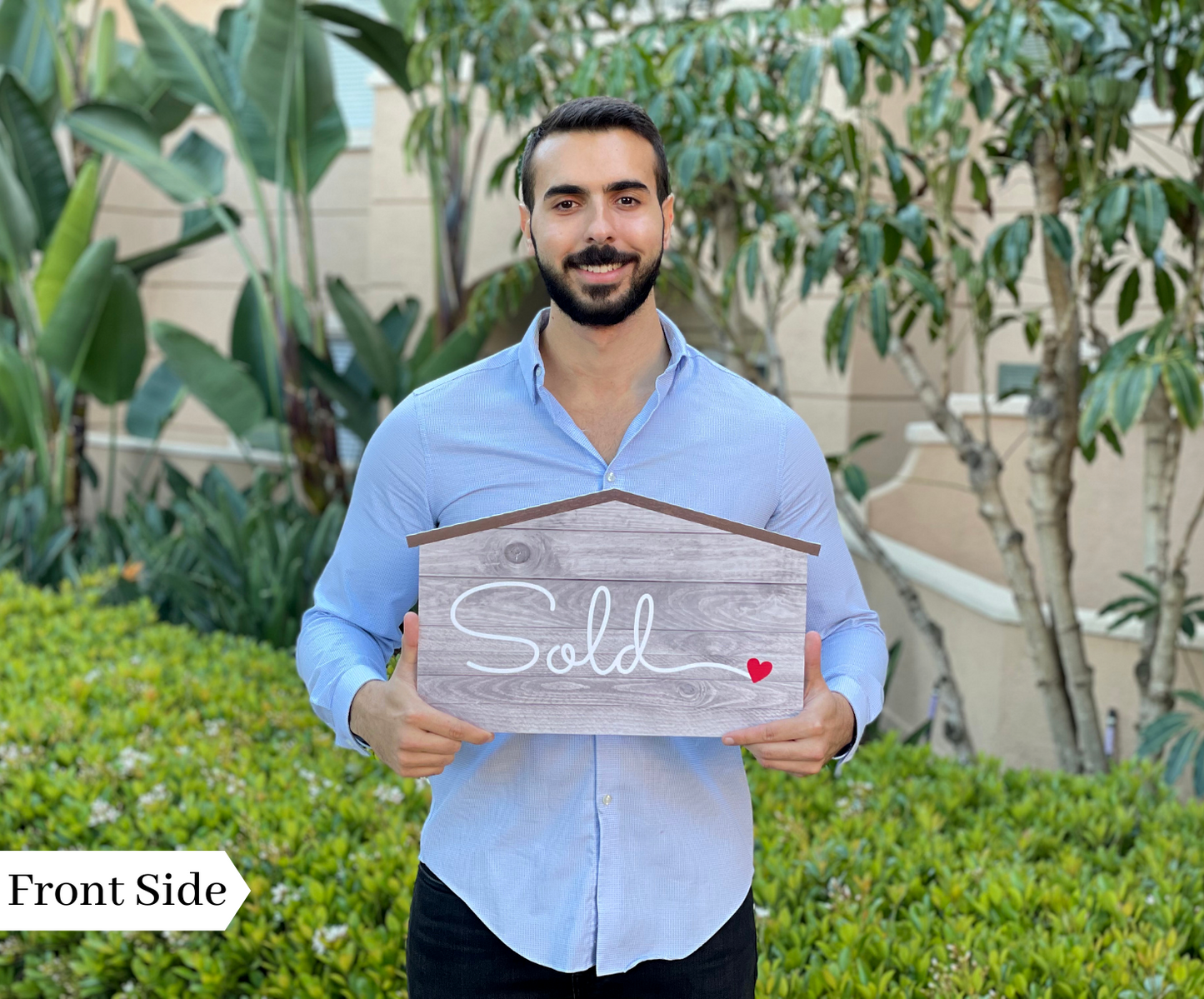 Realtor holding the front side of a rustic wood-style Sold prop sign outdoors