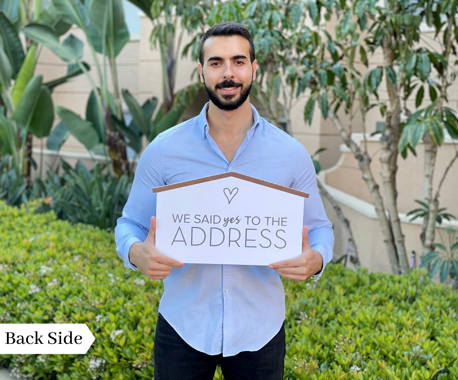 Realtor holding the back side of a rustic wood-style prop sign reading We Said Yes to the Address