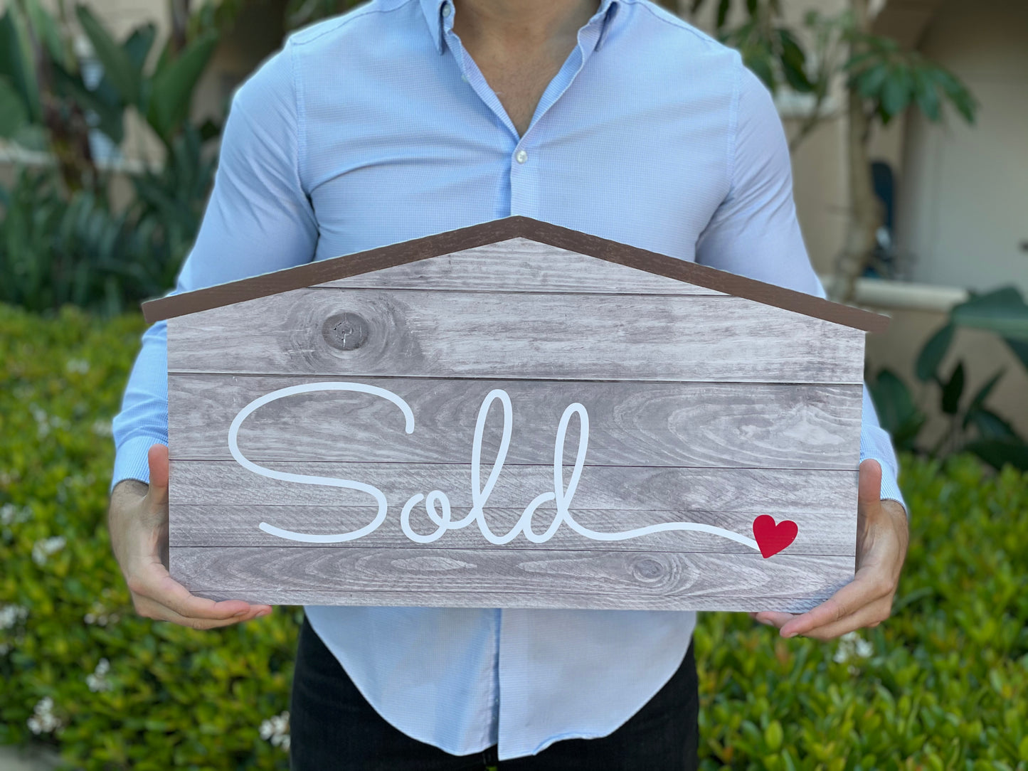 Realtor holding a 24 inch house-shaped Sold sign photo prop in white and brown finish
