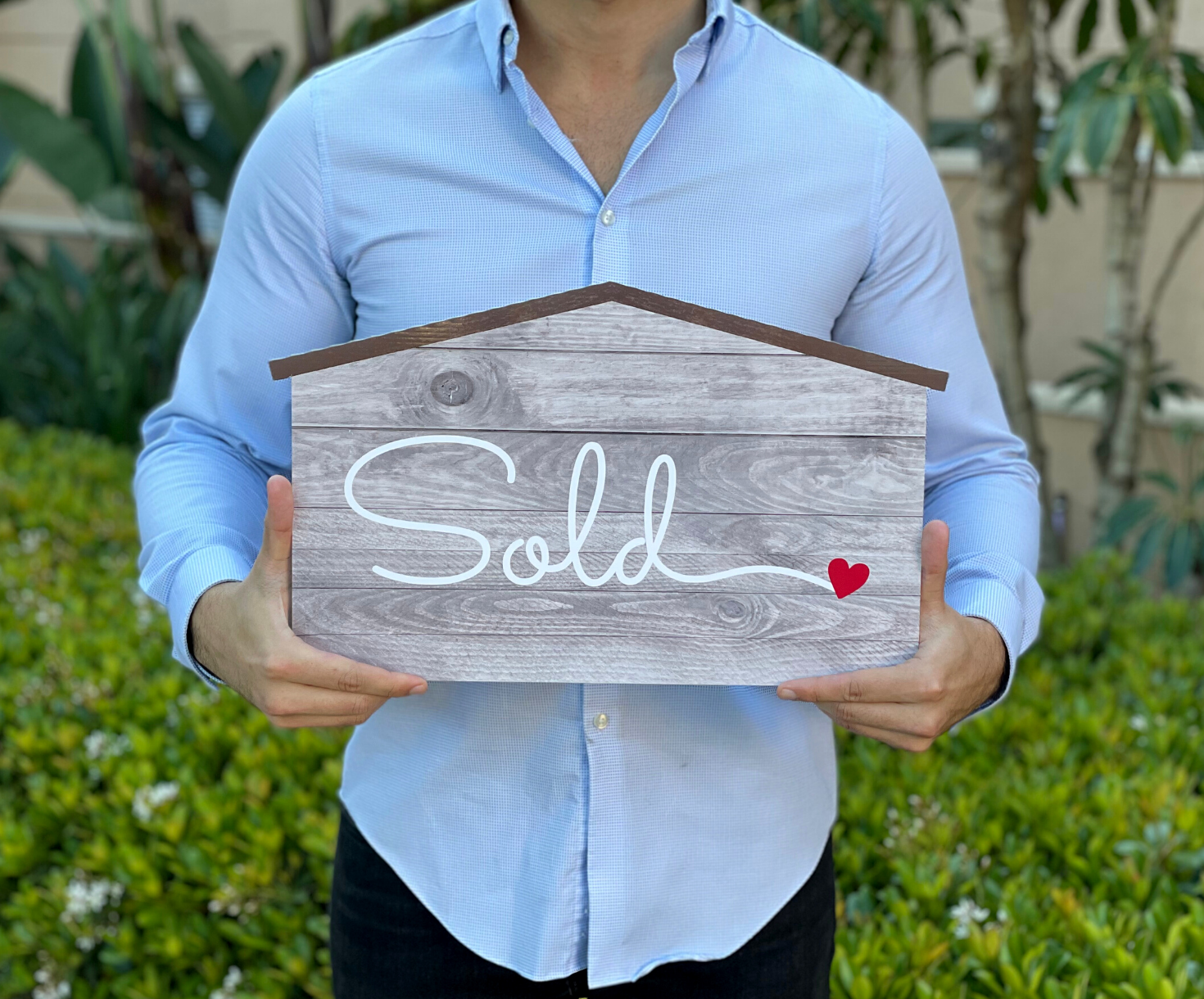 Realtor holding a 17 inch house-shaped Sold sign photo prop in rustic wood-style finish